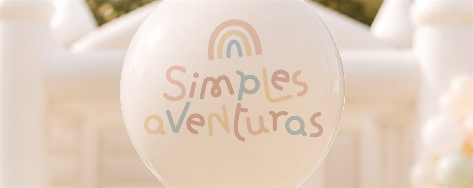 Balão transparente com o logotipo da Simples Aventuras em tons pastel diante de um inflável branco